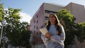 Una estudiante alfrente de la universidad sonríe con los documentos de aplicación