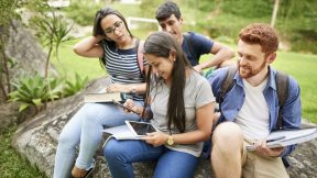 Cuatro estudiantes están sentados juntos en el campus y miran cursos en sus teléfonos celulares.