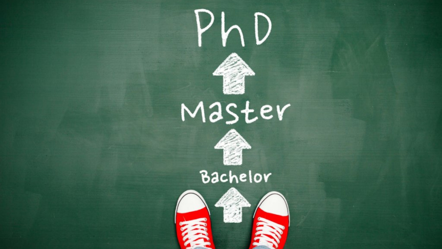 Die Wörter PhD, Master und Bachelor in Kreide geschrieben auf grünem Boden, davor sind rote Turnschuhe zu sehen.