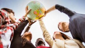 Internationale Studierende halten einen Globus in die Luft.