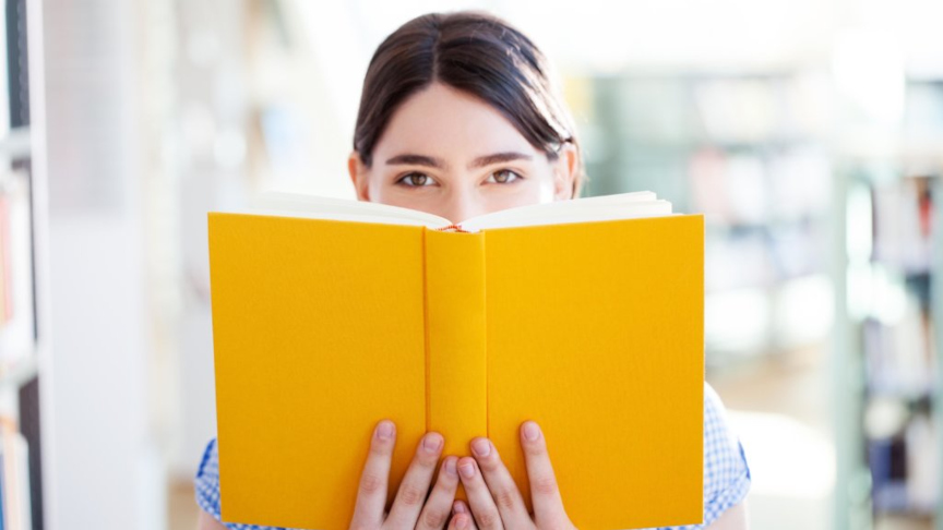 Una joven lee un libro en una biblioteca