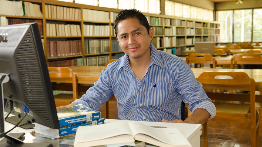 Ein Studierender sitzt vor Büchern in der Bibliothek.