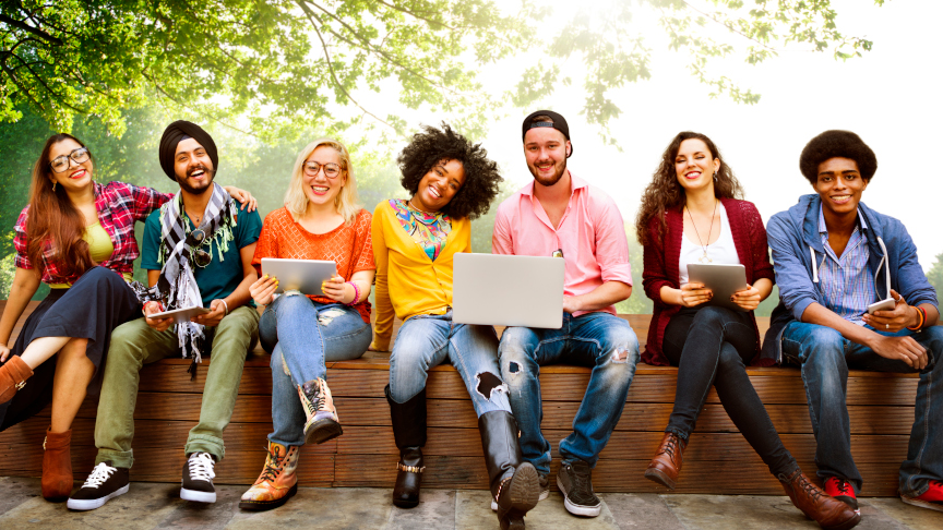 Eine Gruppe junger Menschen mit Laptops sitzt auf einer Bank und lacht